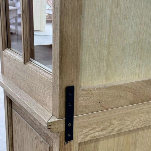 Close-up of a wooden door with black metal hardware, slightly ajar, revealing a French Style Oak Wood Hutch Glass Cabinet inside.