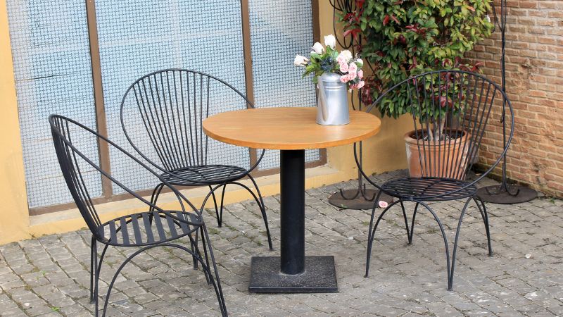 On a cobblestone patio, three metal chairs surround an elegant Hoolnn round table with a metal vase of flowers, "Elevate Your Life.