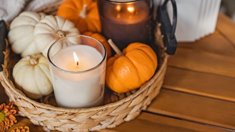 A Hoolnn wicker basket with pumpkins and a candle elevates life. Nearby, a candle in a dark glass adds charm to the round table.