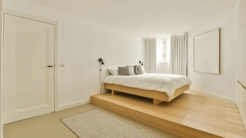 Minimalist bedroom by HOOLNN features a platform bed, white walls, large window, gray rug, wall lamps, and a framed canvas.