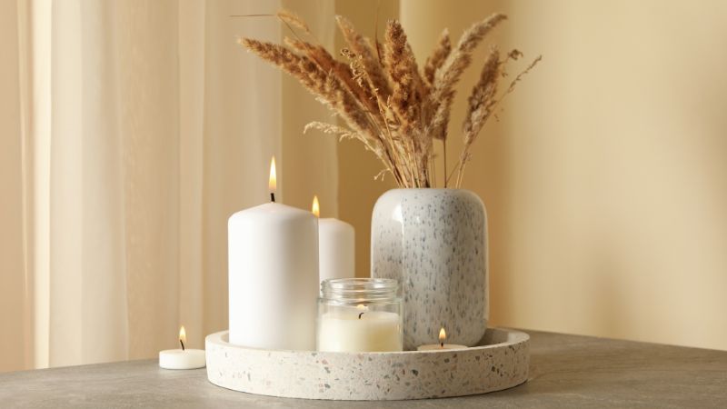 A Hoolnn round tray with candles and a vase of dried grasses elegantly decorates a table against beige curtains.