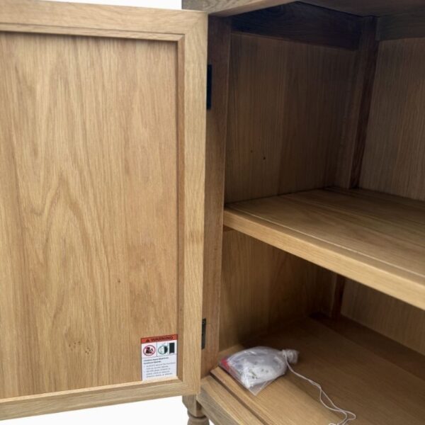 Armoire en bois ouverte avec étiquette d'avertissement à l'intérieur de la porte ; étagères visibles, sachet de gel de silice sur l'étagère inférieure.