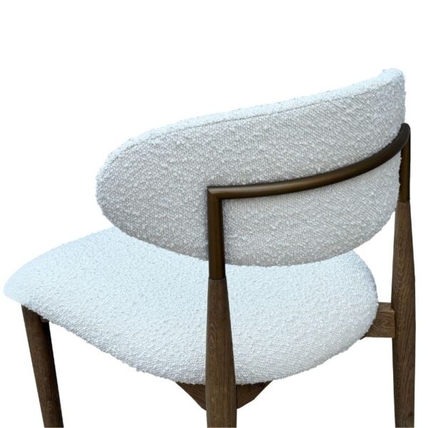 Silla moderna con asiento curvo tapizado en blanco, estructura de metal bronce y patas de madera.