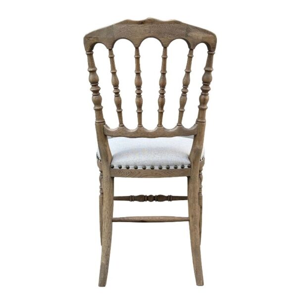 A wooden chair with a spindle back and light upholstered seat, seen from behind.