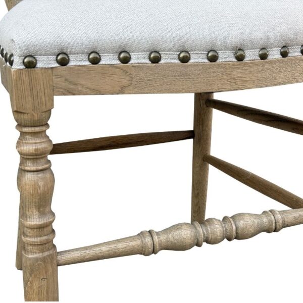 Close-up of a wooden chair leg with turned detail, beige upholstery, and brass nailhead trim along the seat.