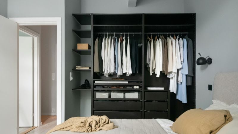 Flexible black wardrobe with organized hanging space and storage drawers in a modern bedroom.
