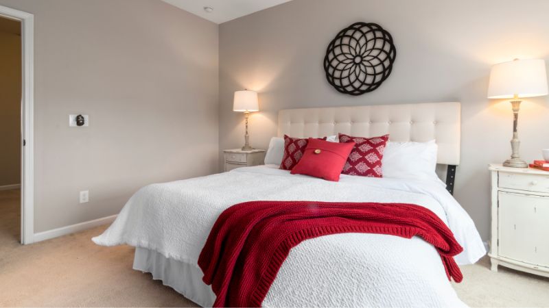 Beautifully decorated bedroom with cozy white bedding, accented by red pillows and blanket, featuring soft lighting and modern decor for a relaxing home atmosphere.