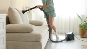 Woman vacuuming a beige linen sofa to remove dust and dirt, maintaining its cleanliness and appearance. Perfect for furniture cleaning and home care tips.