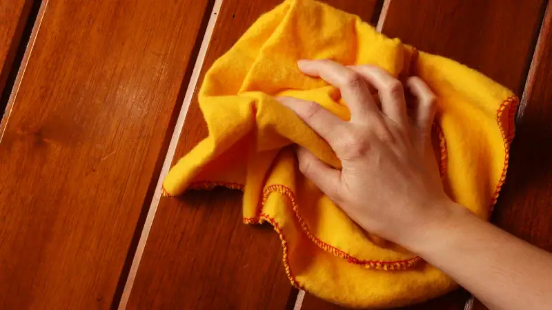 Hand gently cleaning antique wooden furniture with a soft yellow cloth, emphasizing careful maintenance and preservation of vintage wood surfaces.